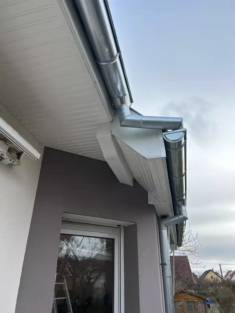 Naissance de descente et gouttière neuves sous un débord habillé de blanc